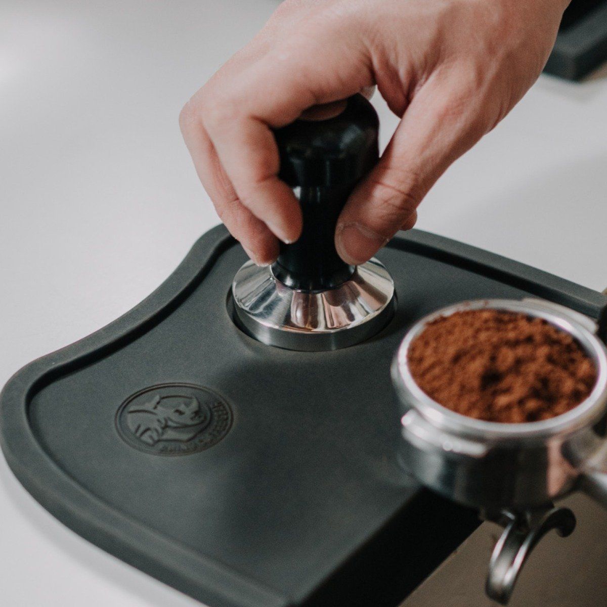 Hand using a coffee tamper on a grinder with ground coffee