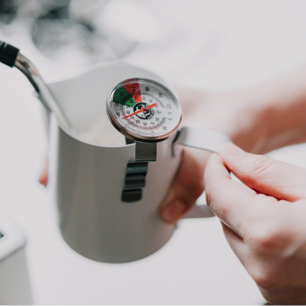 Person using a milk thermometer  on a coffee machine whilst steaming milk