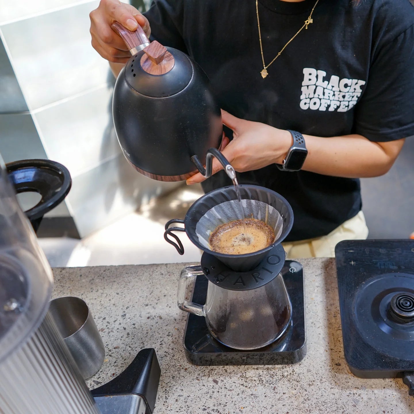 Person pouring coffee from a black kettle into a v60 filter coffee